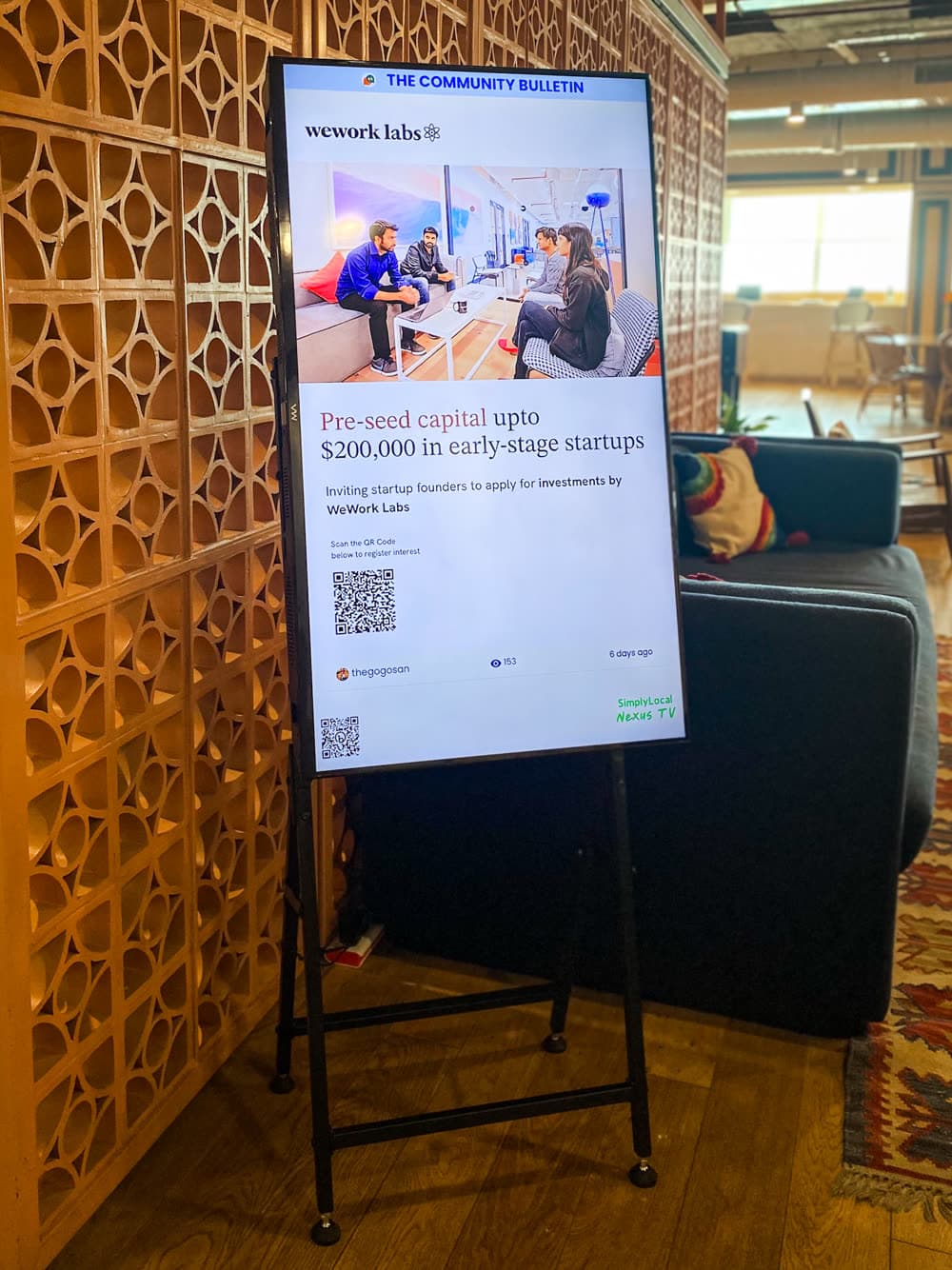 A portrait screen on a stand in a coworking lounge, running a community post